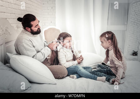 Sorelle e papà seduti sul letto facendo di ogni altri capelli Foto Stock