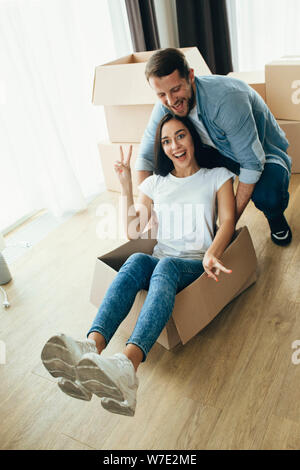 Razza mista giovane divertendosi con scatole di cartone mentre si sposta di nuovo a casa. Foto Stock