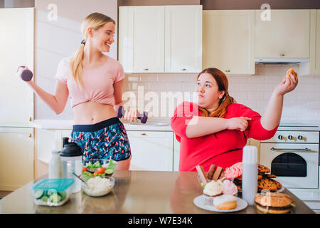 Giovane donna sim holding manubri. Guardando il grasso più dimensioni modello. Corpo positivo. Donna sovrappeso mangiare hamburger e altro cibo spazzatura Foto Stock