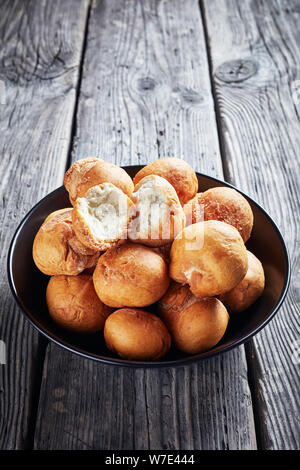 Caraibi fritto gnocchi azzimo in una ciotola nero su un vecchio rustico in legno tabella, vista verticale dal di sopra, close-up Foto Stock