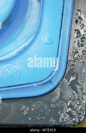 Il bordo di un coperchio di un contenitore di uso domestico dopo la pioggia in blu e nero Foto Stock