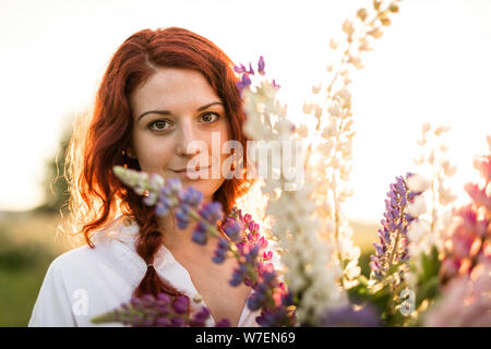 Un bel ritratto di una testa rossa ragazza di nascondersi dietro un mazzo di lupini Foto Stock