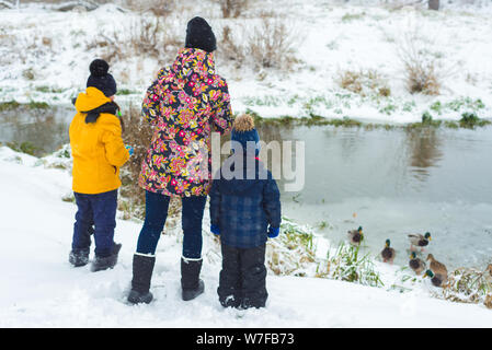 Famiglia mamma e figlia figlio affamati di alimentazione anatre in inverno su un lago ghiacciato Foto Stock