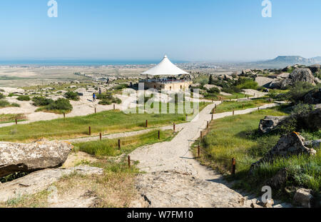 Gobustan, Azerbaigian - 1 maggio 2019. Paesaggio in Gobustan national park, con percorsi, Pavilion, di persone e di Gobustan insediamento nella distanza. Foto Stock