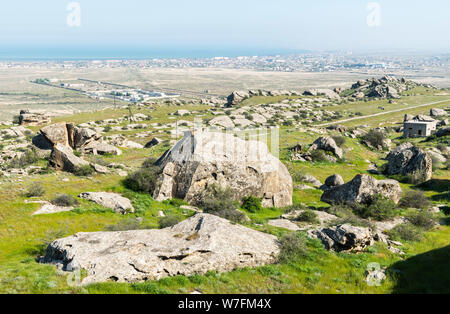 Paesaggio in Kichikdash area di Gobustan, Azerbaigian, con pile di boulder e di Gobustan carcere e di insediamento in background. Foto Stock