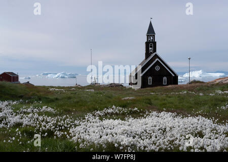 La Chiesa di Sion in Ilulissat, circondato da fiori e con gli iceberg della baia di Disko in background. Foto Stock