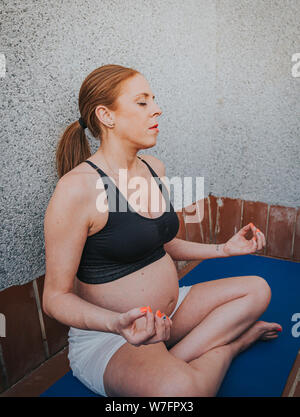 Donna incinta fare yoga sul tappetino fitness nel tetto Foto Stock