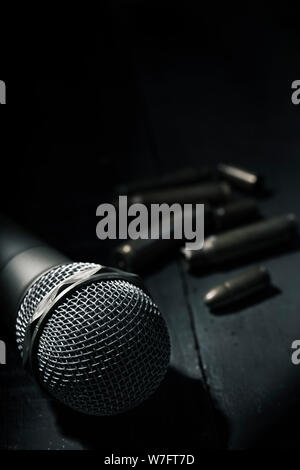 Primo piano di un microfono su un grigio scuro superficie rustico e alcune pallottole e bullet gusci in background, con qualche spazio vuoto sulla parte superiore Foto Stock