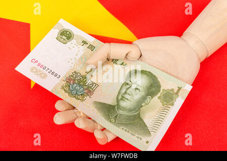 Yuan cinese banconota in legno / manichino manichino in mano con bandiera della Cina. Metafora Donald Trump il riferimento alla Cina la manipolazione di valuta. Foto Stock