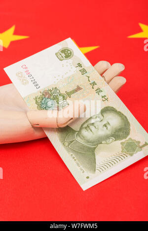 Yuan cinese banconota in legno / manichino manichino in mano con bandiera della Cina. Metafora Donald Trump il riferimento alla Cina la manipolazione di valuta. Foto Stock