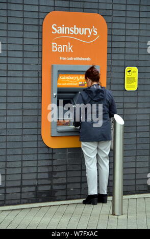 Una donna adulta usando un Sainsbury's Bank atm in Stockport, Greater Manchester Foto Stock