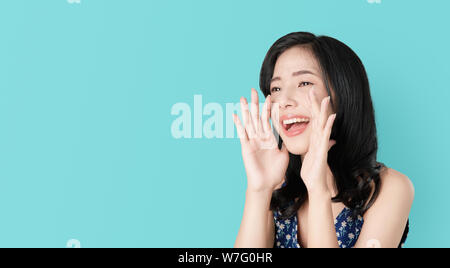 Attraente giovane donna asiatica annunciando con le mani alla bocca e raccontare un segreto, isolata su fondo azzurro Foto Stock