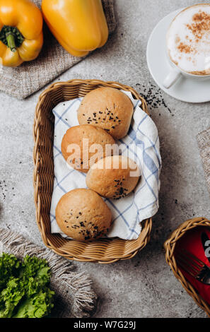 Panini dolci con semi di papavero per la colazione su uno sfondo grigio con insalata. Foto Stock