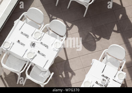 Tavoli e sedie bianchi stand ad un vuoto di una terrazza esterna, vista dall'alto Foto Stock