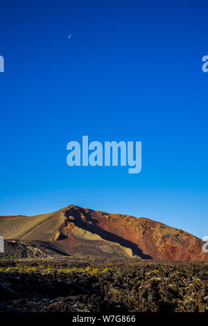 Spagna Lanzarote, impressionante colorato di rosso il cratere vulcanico e Luna in early sunrise light Foto Stock