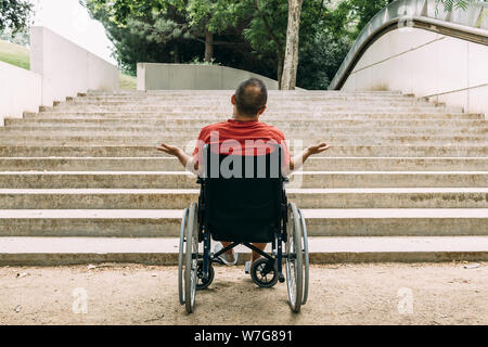 Uomo disabili su sedia a rotelle arrestato indignato di fronte a scale che non sono in grado di salire in cerca di aiuto, sensibilizzazione delle barriere architettoniche e acces Foto Stock