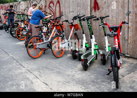 Elettrico a due ruote. E-scooter e batteria-powered biciclette disordine città marciapiedi fuori il palazzo della città nel quartiere Mitte di Berlino. Foto Stock