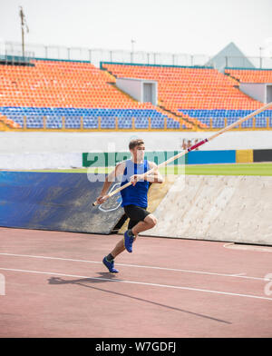 Pole Vault - un giovane uomo corre fino tenendo un palo in stadium Foto Stock