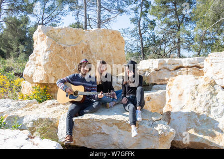 Un gruppo di giovani felici hanno avente un barbecue in natura e cantare intorno a un chitarrista Foto Stock