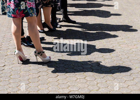 Gambe di festosa vestita di persone in piedi in fila, con le loro ombre Foto Stock