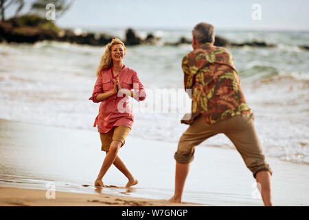 Coppia sulla spiaggia scherzosamente prendendo le foto di ogni altro. Foto Stock