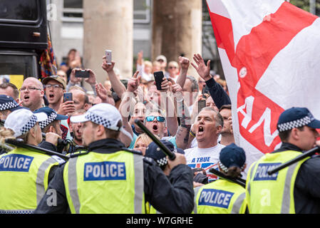 Una folla di persone in collera a libero Tommy Robinson rally di protesta a Londra, Regno Unito, dietro il cordone di polizia. Inghilterra bandiera. La polizia manganelli sollevato Foto Stock