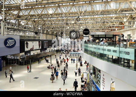 Passeggeri e pendolari che camminano lungo l'atrio Negozio di stivali sotto l'orologio nella stazione di Waterloo a Londra INGHILTERRA REGNO UNITO KATHY DEWITT Foto Stock