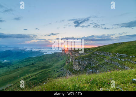 Tramonto in montagna. Il sole che illumina la gamma della montagna, nebbia e nuvole. Foto Stock