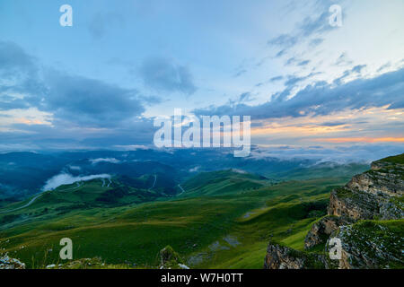 Si illumina al tramonto le nuvole sopra una montagna verde valle nella nebbia Foto Stock