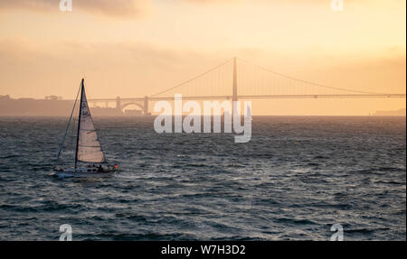 Il Golden Gate Bridge di San Francisco, California al tramonto con un piccolo yacht vela passato Foto Stock