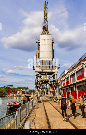 La gente camminare passato Bristol M-Shed museo l'Harbourside accanto a 1950 electric gru portuali. Bristol, Regno Unito. Luglio 2019. Foto Stock