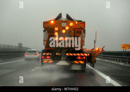 Autostrada manutenzione carrello gritter diffusione de-icing, sale sul ghiaccio coperto strada asfaltata durante il giorno nuvoloso Foto Stock