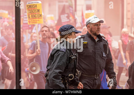 Agente di polizia donna all'opposizione a una manifestazione di protesta di Free Tommy Robinson a Londra, Regno Unito, con fumo da flare. Ufficiale sergente maschile in berretto bianco Foto Stock