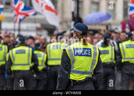 Una folla di persone in collera a libero Tommy Robinson rally di protesta a Londra, Regno Unito, dietro il cordone di polizia. Separare lone funzionario femmina dietro la linea dei maschi Foto Stock