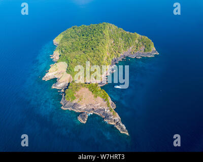 Una sola barca accanto a un telecomando, disabitata isola tropicale coperta nella giungla verde e circondato da tropical Coral reef Foto Stock