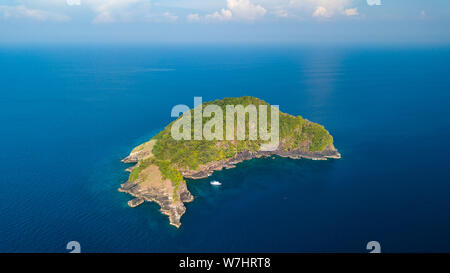 Una sola barca accanto a un telecomando, disabitata isola tropicale coperta nella giungla verde e circondato da tropical Coral reef Foto Stock