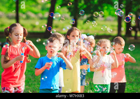 Un gruppo di bambini che giocano con le bolle di sapone all'esterno. Amici cercando  di catturare le bolle Foto stock - Alamy