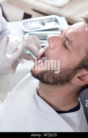 Dentista fa un'iniezione con anestesia in gomma del paziente. Un uomo di faccia con una bocca aperta su un riunito dentale. Foto Stock