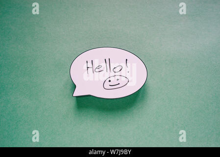 Discorso bolla segno con le parole ciao e sorridente. Messaggio vocale simbolo della carta su sfondo verde. Biglietto di auguri o un invito. Foto Stock