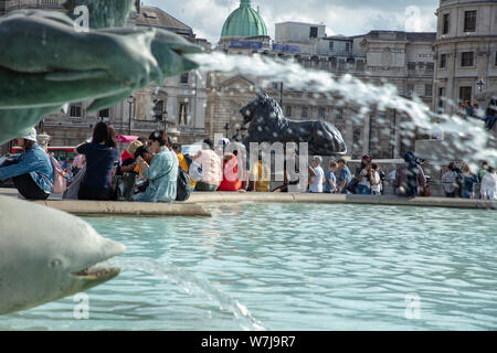 Tourist seduta sul bordo del bacino circostante di una fontana a Trafalgar Square in un caldo pomeriggio d'estate in agosto. Foto Stock