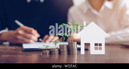 Le coppie hanno firmato un contratto per acquistare una casa da broker. Coin alla pila di denaro e modello di casa collocata sul tavolo, finanziario la crescita del business. Foto Stock