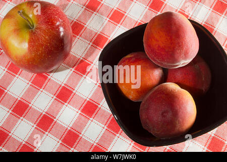 Le pesche in un piatto di ceramica su un tovagliolo a scacchi Foto Stock