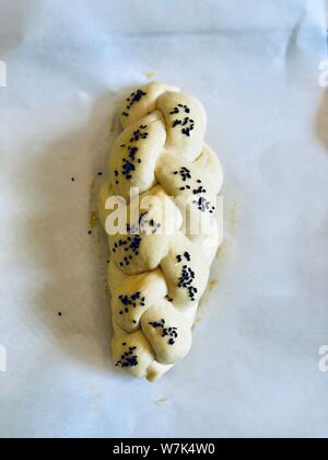 Challah pane di pasta intrecciata prima della sua cotta su una carta di rinforzo in casa Foto Stock