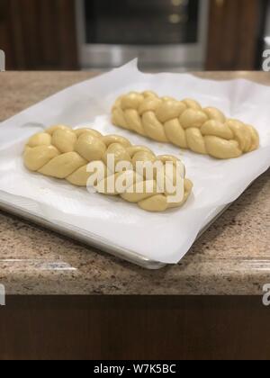 Supporto challah in casa pane di pasta intrecciata prima della sua cotta su una carta di rinforzo Foto Stock