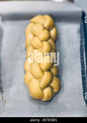 Supporto challah in casa pane di pasta intrecciata prima della sua cotta su una carta di rinforzo Foto Stock