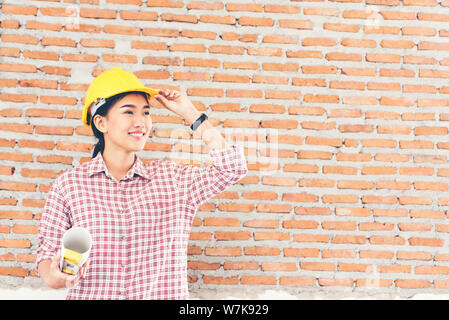 Bella giovane ingegnere di lavoro tenendo i progetti di un edificio indossare casco giallo. Foto Stock