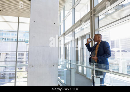 Imprenditore di bere il caffè in piedi in un moderno edificio per uffici Foto Stock