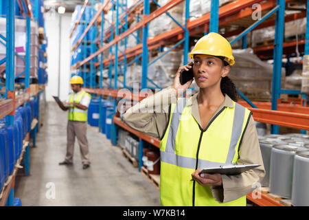Lavoratore di sesso femminile che holding negli appunti e parlando al telefono cellulare in magazzino Foto Stock