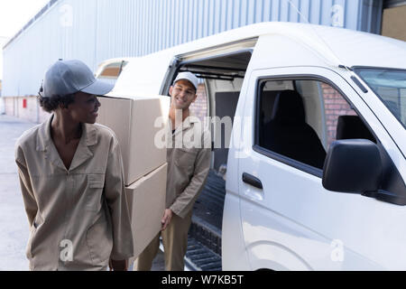 Consegna l uomo e la donna che trasportano le scatole di cartone vicino a van al di fuori del magazzino Foto Stock