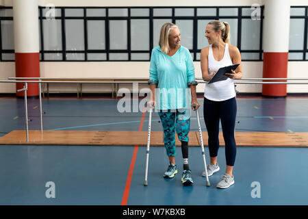 Fisioterapista femmina di parlare con persone con disabilità senior donna nel centro sportivo Foto Stock